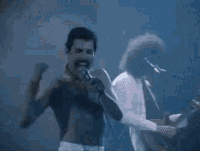 a man is singing into a microphone while another man plays a guitar in a band .
