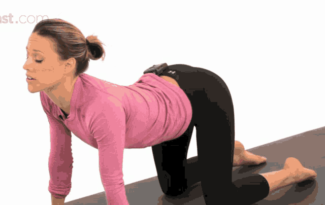 a woman in a pink shirt and black pants is kneeling on a yoga mat