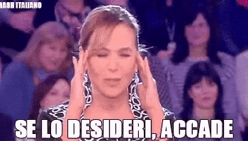 a woman is holding her head in front of a crowd of people and says `` se lo desideri accade '' .
