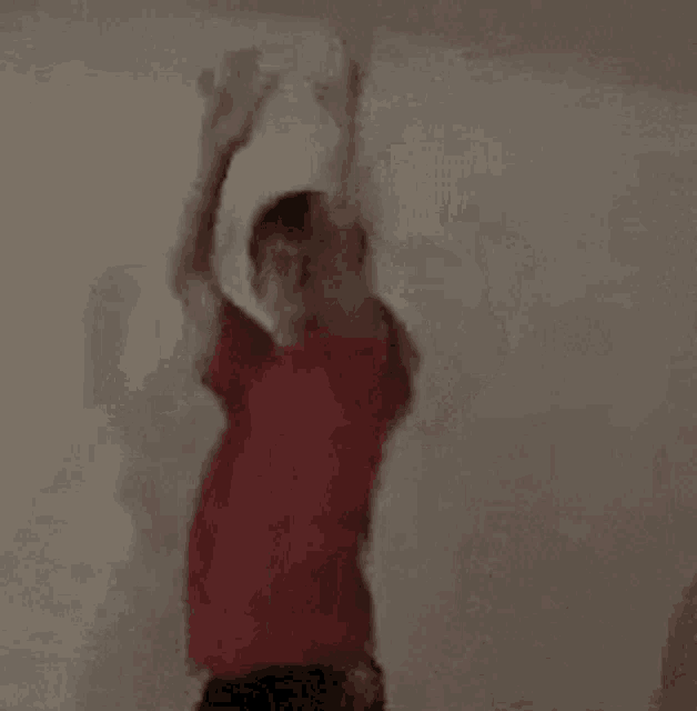 a young boy in a red shirt and black shorts is dancing in a dark room .