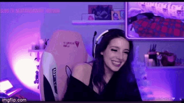 a woman is sitting in a pink gaming chair with headphones on and smiling .