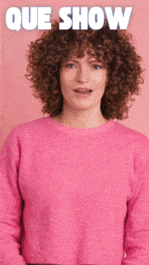 a woman with curly hair is wearing a pink sweater and the word que show is above her