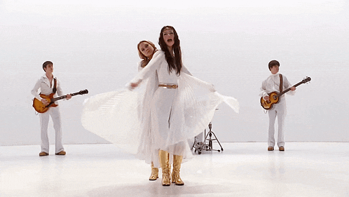a woman in a white dress is standing in front of a group of people playing guitars