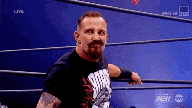 a man with a beard is standing in a wrestling ring and pointing at something .