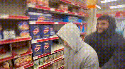 a man in a hoodie is standing in front of a grocery store shelf .