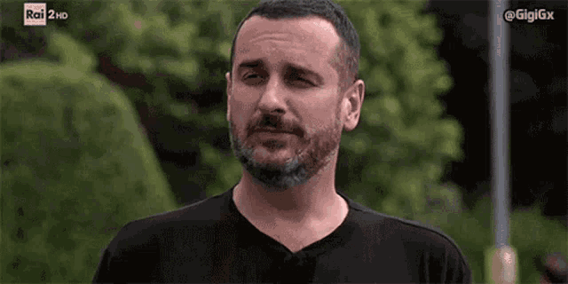 a man with a beard is wearing a black shirt and making a funny face .