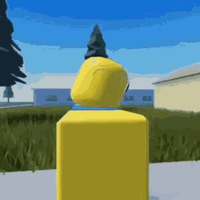 a yellow roblox character is standing in front of a house and trees .