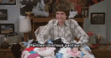 a man is sitting on a bed with a pile of underwear and says panties ! glorious panties !
