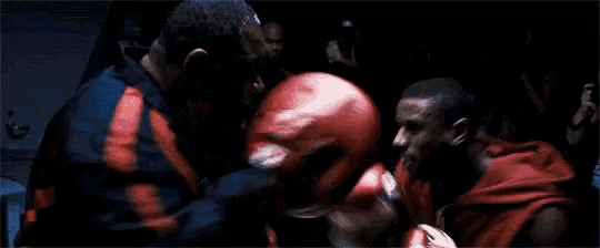 two men are boxing in a dark room and one of them is wearing red gloves .