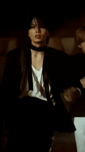 a man in a black jacket and white shirt is standing in the dark .