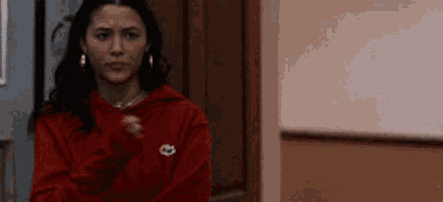 a woman in a red hoodie is standing in a hallway and making a funny face .