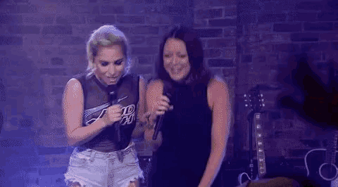 a couple of women are standing next to each other on a stage holding microphones .