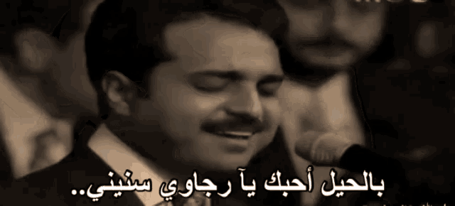 a man in a suit singing into a microphone with arabic writing on it
