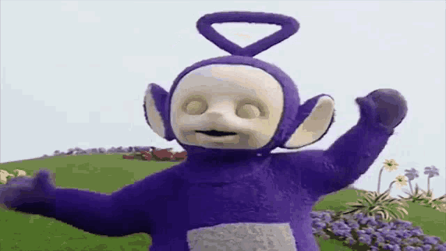 a purple teletubbies doll is standing in a field with his arms outstretched .