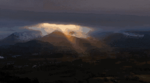 the sun shines through the clouds over a mountain range