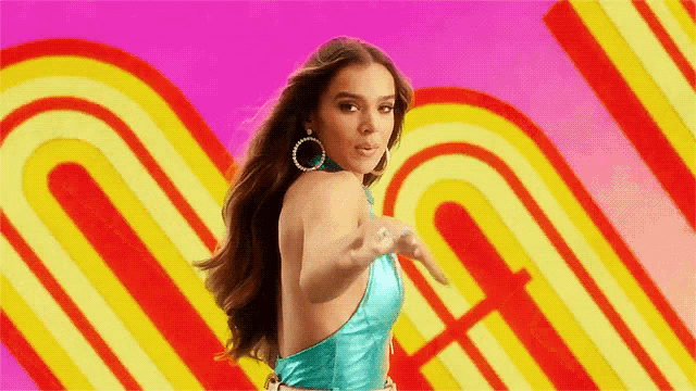 a woman in a blue top is dancing in front of a pink and yellow background