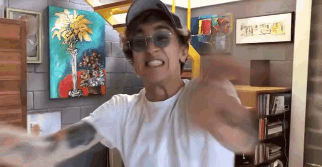 a man wearing sunglasses and a hat is smiling in front of a painting