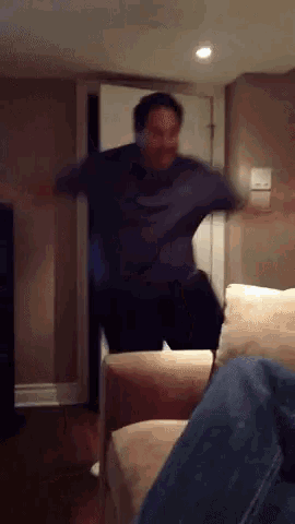 a man in a blue shirt is jumping in a living room