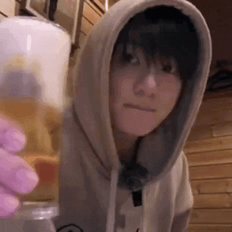 a man wearing a hoodie is holding a glass of beer .