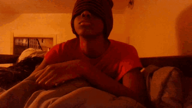 a young man wearing a red shirt and a beanie is laying on a bed