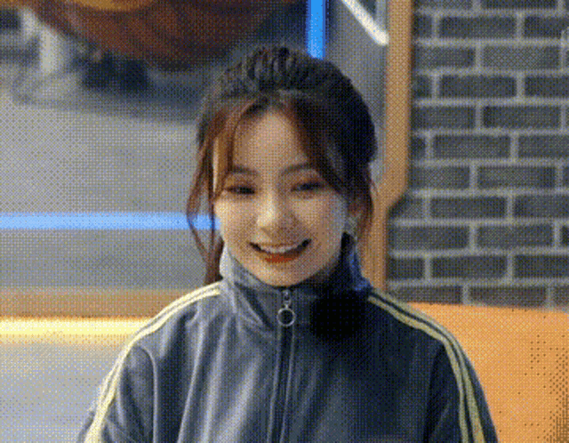 a close up of a woman wearing a gray jacket and smiling in front of a brick wall .