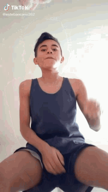a young boy in a tank top and shorts is making a funny face