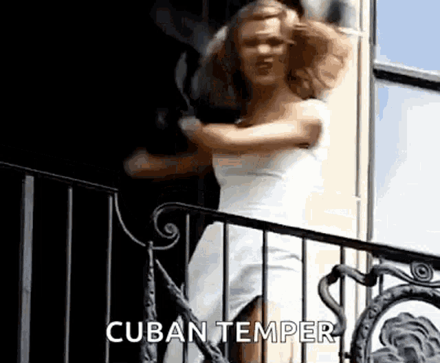 a woman in a white dress is standing on a balcony with her arms outstretched .