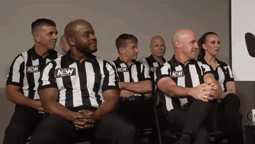 a group of men wearing aew shirts sit in a row