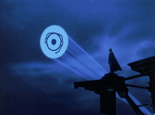 a man in a cape stands on top of a building in front of a blue circle with the letter o coming out of it