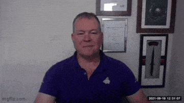 a man in a purple shirt is standing in front of a wall with pictures on it .