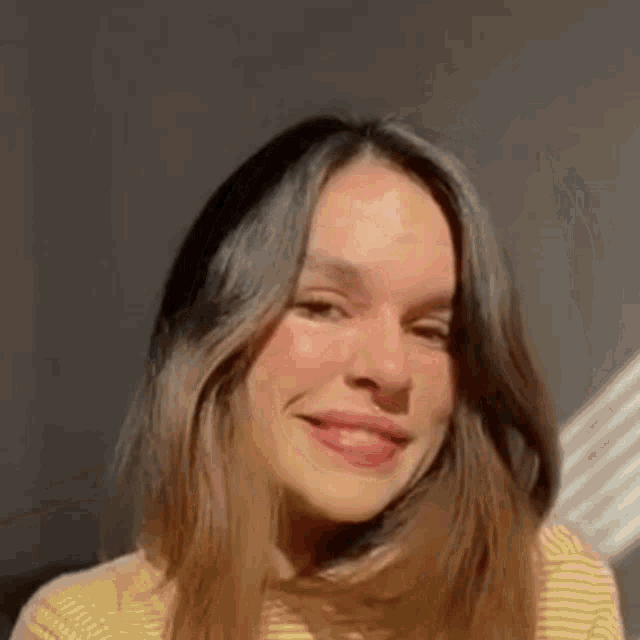 a woman with long hair is smiling for the camera while wearing a striped sweater .