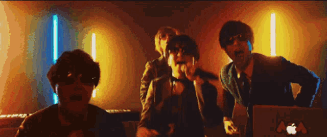 a group of people are dancing in front of a keyboard and an apple computer