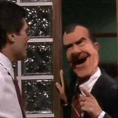 a man in a suit and tie is talking to another man in a mask