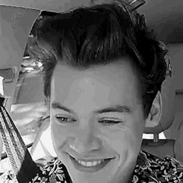 a black and white photo of harry styles smiling in a car .