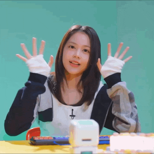 a girl with a cross on her chest is sitting at a table with her hands up