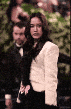 a woman in a white jacket stands in front of a man in a tuxedo