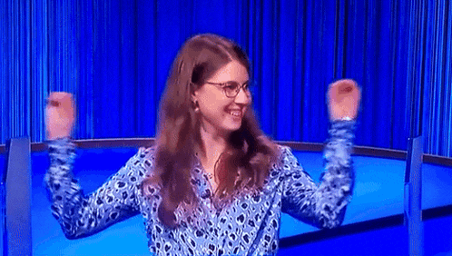 a woman wearing glasses and a blue shirt is raising her arms in the air .