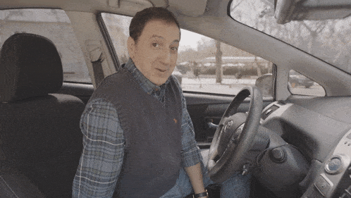a man in a plaid shirt sits in the driver 's seat of a toyota prius