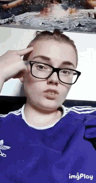 a girl wearing glasses and a blue adidas shirt takes a selfie