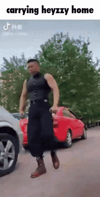 a muscular man is carrying a red car in a parking lot ..