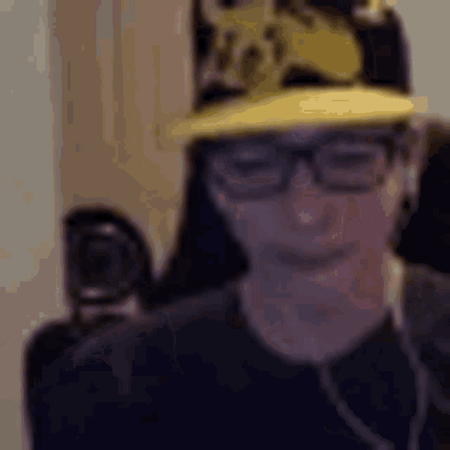 a man wearing glasses and a yellow hat is sitting in a chair .