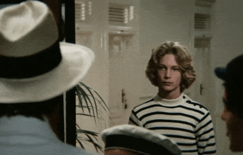 a man wearing a striped shirt and a hat stands in a room