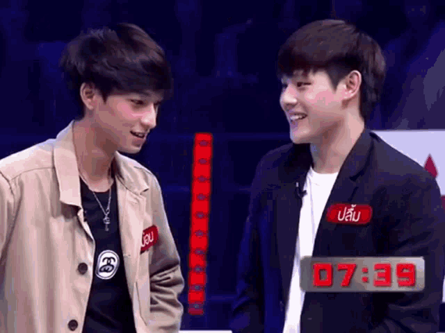 two young men are standing next to each other with the time of 7:39 on the screen behind them