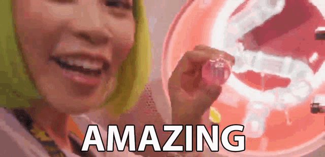 a woman with green hair is holding a pink object in front of a neon sign that says ' amazing ' .