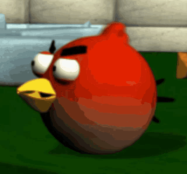 a red angry bird with a yellow beak is sitting on a green surface