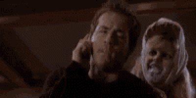 a man is talking on a cell phone while a woman kisses him on the forehead .