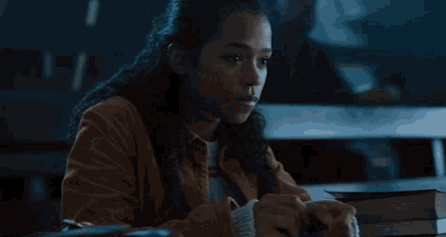 a girl with curly hair is sitting at a desk with a stack of books