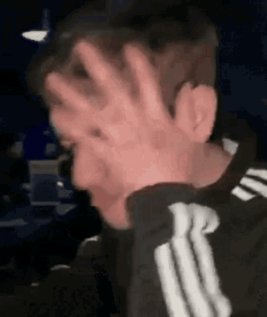 a man covering his face with his hands in a dark room .