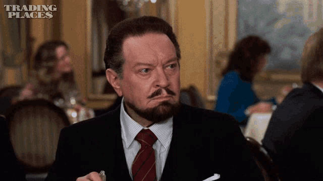 a man in a suit and tie is sitting at a table with trading places written in the corner