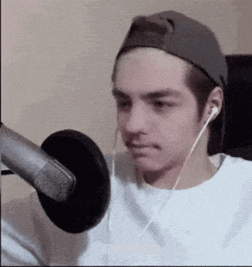 a man wearing headphones and a hat is sitting in front of a microphone .